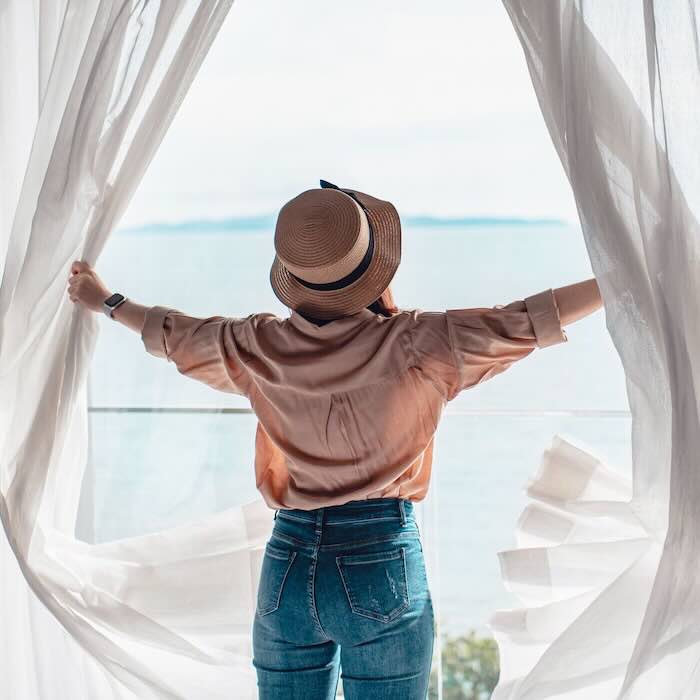 Woman enjoying ocean view through open curtains.